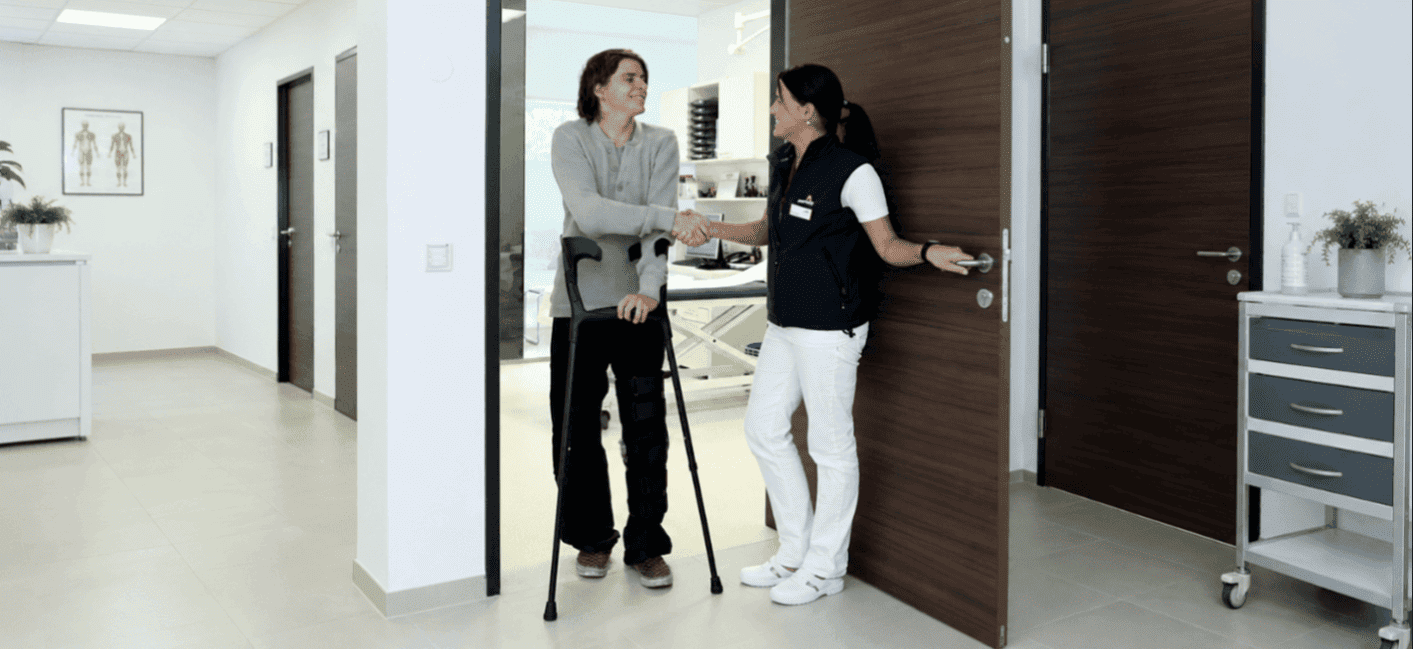 Man sieht zwei Personen im Gang einer Klinik. Ein Mann mit Krücken drückt einer Ärztin die Hand.