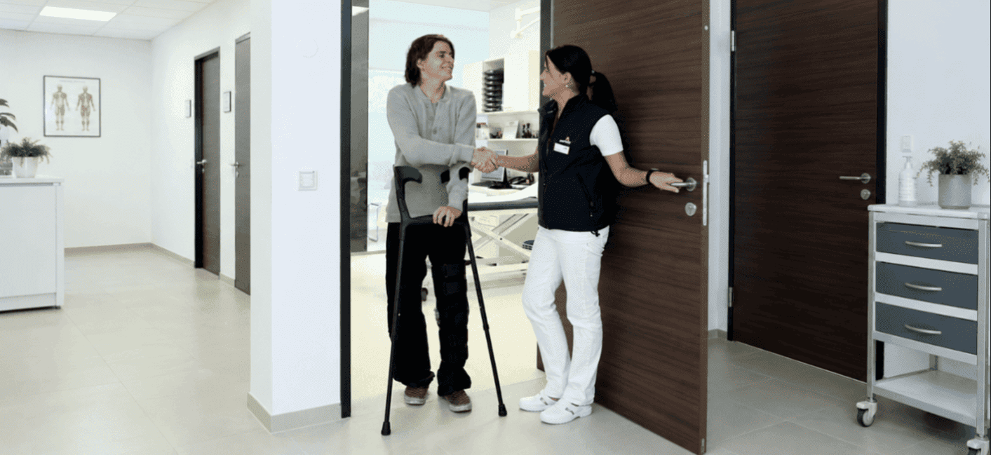 Man sieht zwei Personen im Gang einer Klinik. Ein Mann mit Krücken drückt einer Ärztin die Hand.