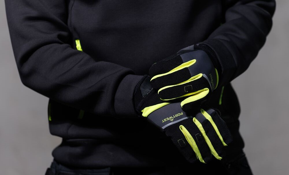 Ein Arbeiter in schwarzem Sweatshirt zieht sich ein Paar DX4 LR Schnittschutzhandschuhe A774 in Gelb und Schwarz an.