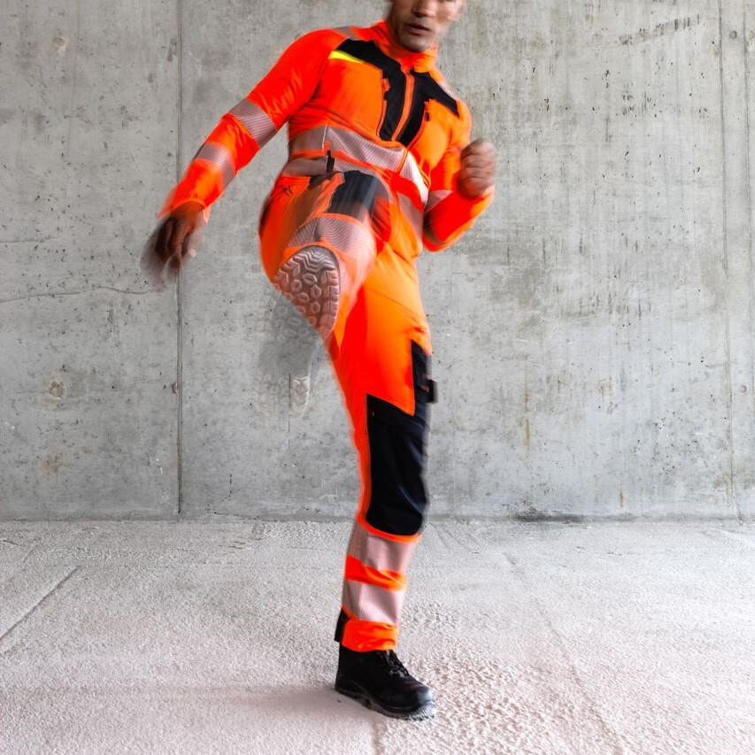 Arbeiter in oranger Schutzkleidung hat ein Bein in einem Kick erhoben.