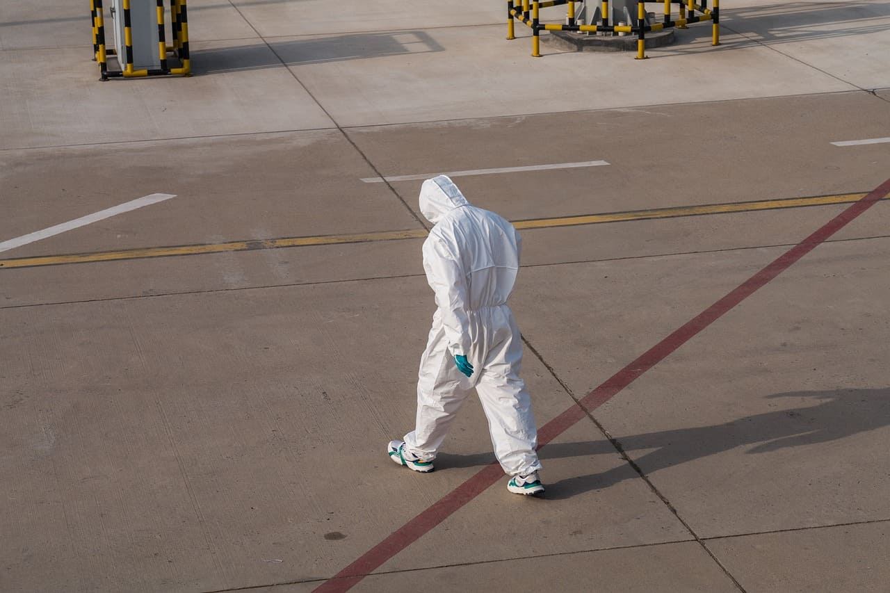 Eine Person in weißem Einwegoverall und blauen Einweghandschuhen läuft über ein Flugfeld.