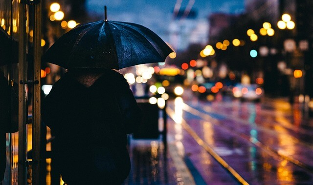 Verregnete Straßenszene im Dunkeln. Eine Person unter einem Regenschirm befindet sich im linken Bildbereich.