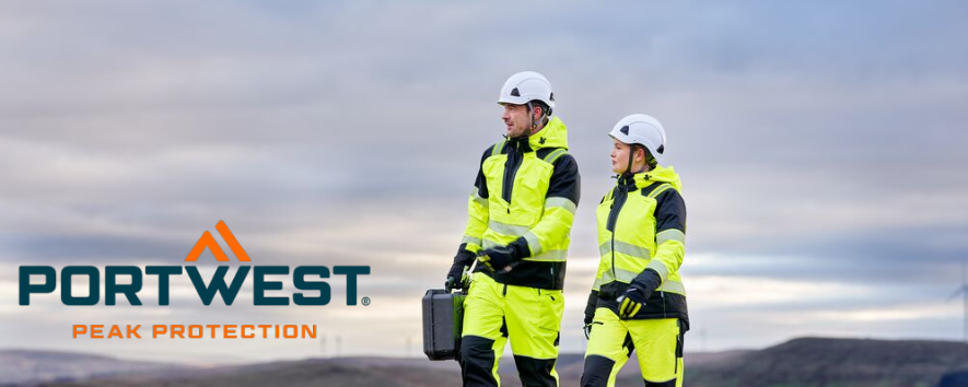 Das Bild zeigt einen Mann und eine Frau in gelber Arbeitskleidung und wei&szlig;en Schutzhelmen. Sie laufen auf einem Schotterweg. Im Hintergrund sieht man eine H&uuml;gelkette und einen blauen Himmel mit Wolken. Das blau-orange Logo des Herstellers Portwest befindet sich im linken unteren Eck.