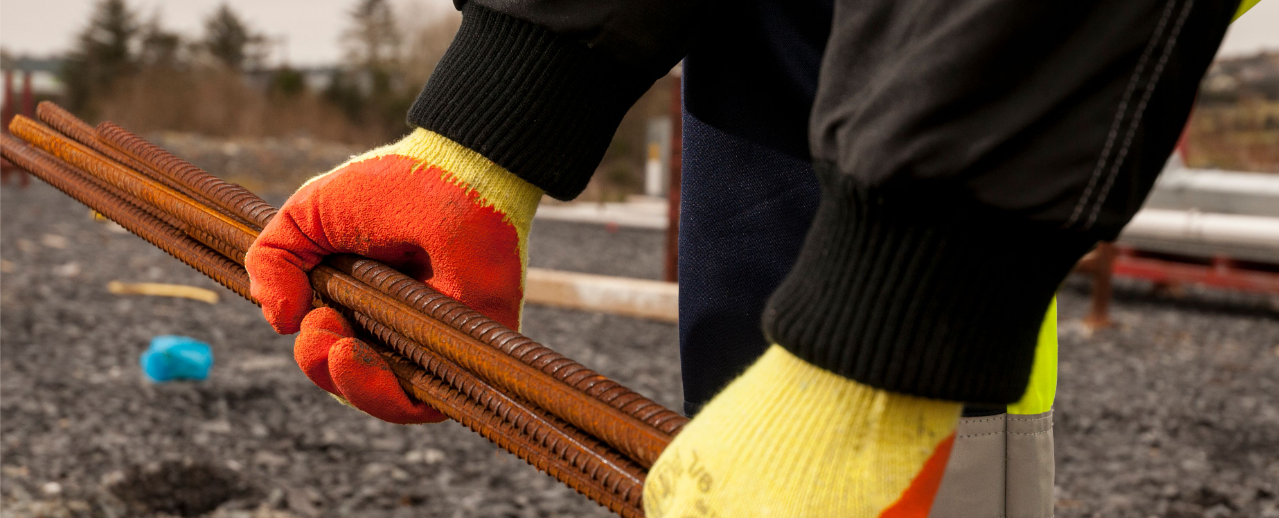 Modellbild des Fortis Grip Handschuhs A150 in Gelb/Orange bei der Arbeit mit Armierungseisen.