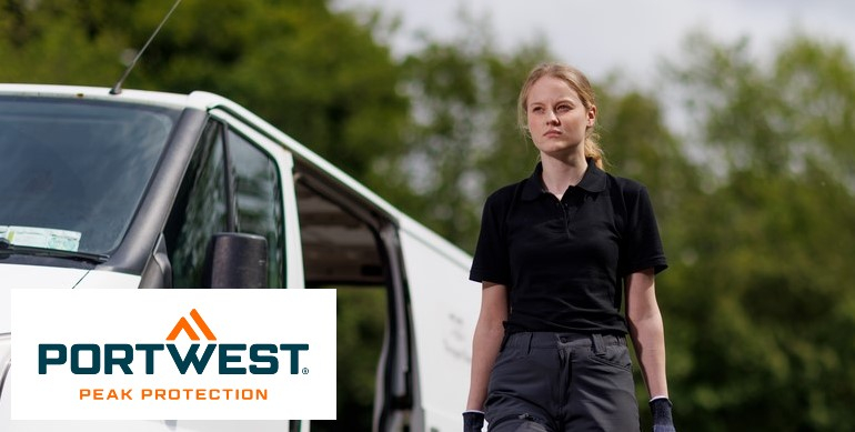 Eine Frau in einem schwarzen Polo-Shirt und grauen Arbeitshosen steht vor einem weißen Lieferwagen im Freien. Im Hintergrund sind grüne Bäume zu sehen. Unten links im Bild befindet sich das Logo von "Portwest Peak Protection".