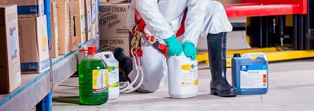 Person in weißem Schutzanzug mit Handschuhen und Sicherheits-Gummistiefeln bei der Arbeit mit Chemikalien.