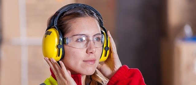 Frau in Arbeitskleidung mit Gehörschutz und Schutzbrille.