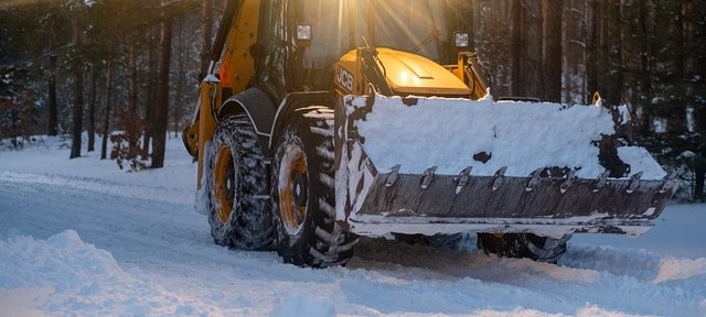 Symbolbild Winter mit einem Schaufelbagger auf einem verschneiten Waldweg.